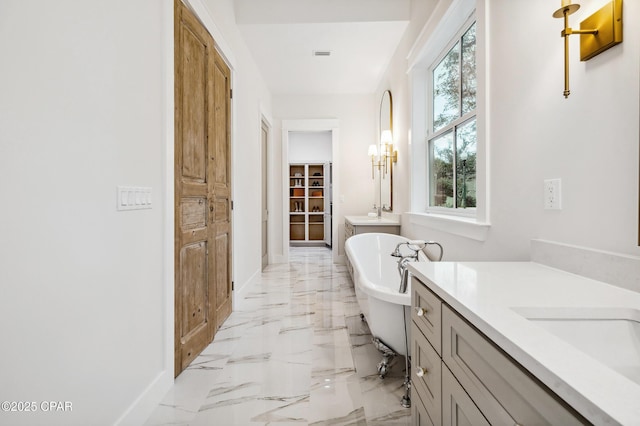 bathroom featuring baseboards, a soaking tub, two vanities, marble finish floor, and a closet