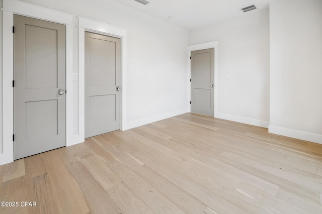 spare room with light wood-type flooring, visible vents, and baseboards