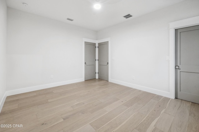 empty room with light wood finished floors, baseboards, and visible vents