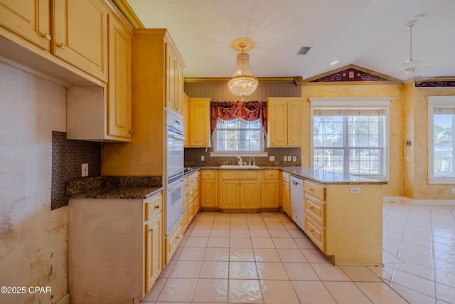 kitchen with hanging light fixtures, dark stone countertops, light brown cabinetry, and white appliances