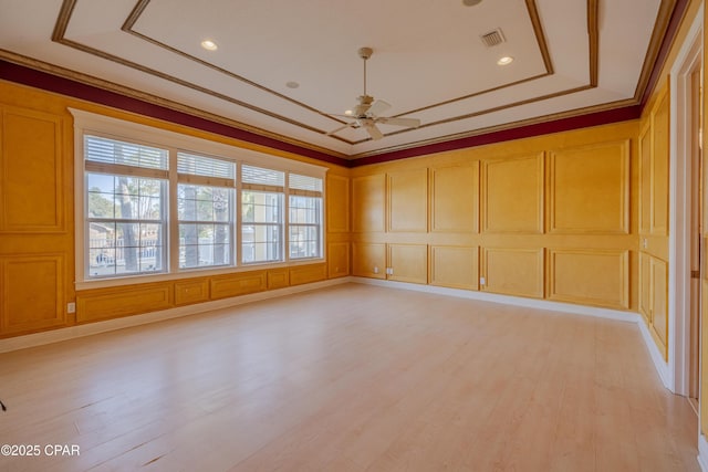 empty room featuring crown molding, ceiling fan, a tray ceiling, and light hardwood / wood-style flooring