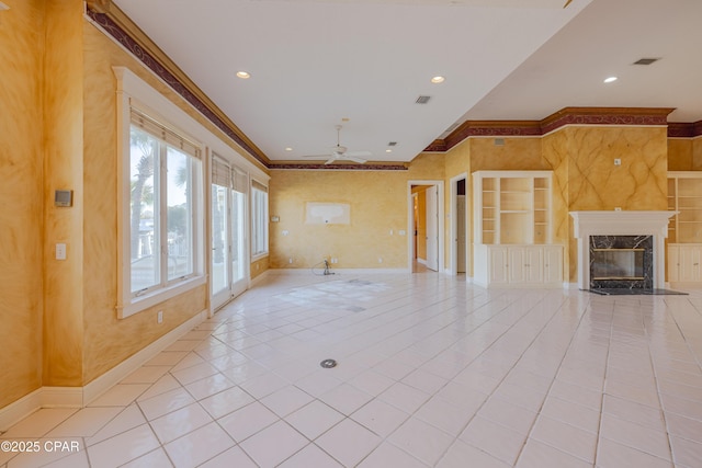 unfurnished living room with light tile patterned floors, ceiling fan, a high end fireplace, crown molding, and built in shelves