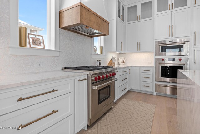 kitchen with appliances with stainless steel finishes, custom range hood, white cabinets, and light stone counters