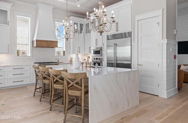 kitchen featuring stainless steel appliances, an island with sink, white cabinets, and premium range hood