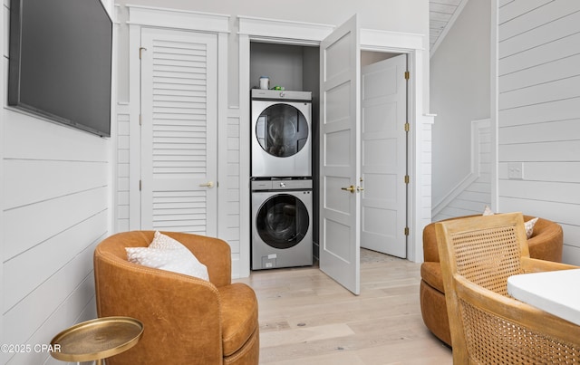 washroom featuring stacked washer and dryer, light hardwood / wood-style flooring, and wood walls