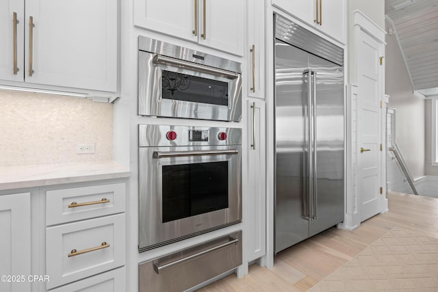 kitchen featuring light hardwood / wood-style flooring, backsplash, stainless steel appliances, light stone counters, and white cabinets