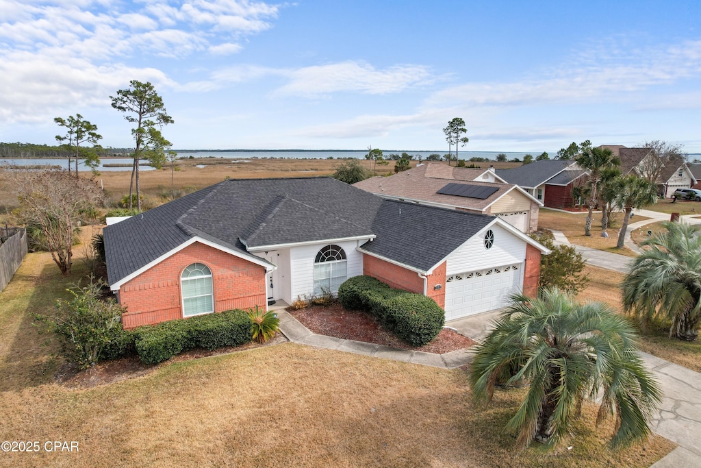 view of front of home featuring driveway, a garage, a shingled roof, a water view, and brick siding