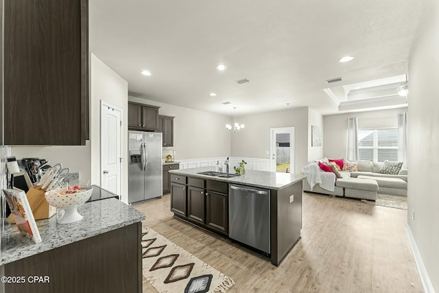 kitchen with light wood finished floors, stainless steel appliances, open floor plan, dark brown cabinetry, and a sink