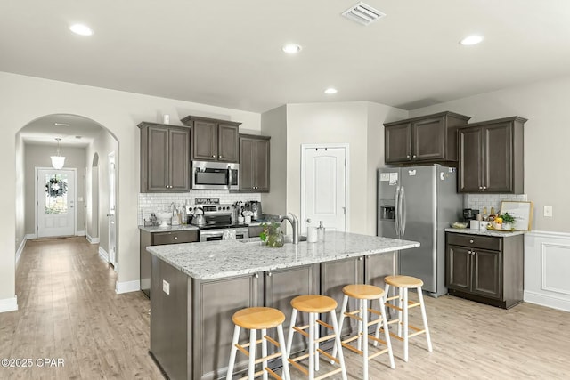 kitchen featuring arched walkways, stainless steel appliances, visible vents, light wood-style floors, and a sink