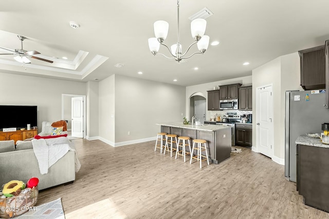 kitchen with arched walkways, stainless steel appliances, a breakfast bar, light wood-style floors, and open floor plan