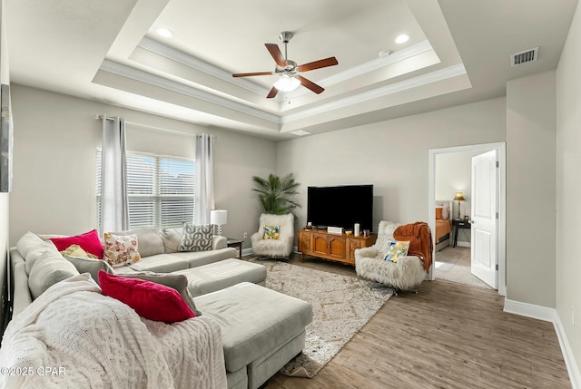 living room with visible vents, ornamental molding, a tray ceiling, and wood finished floors