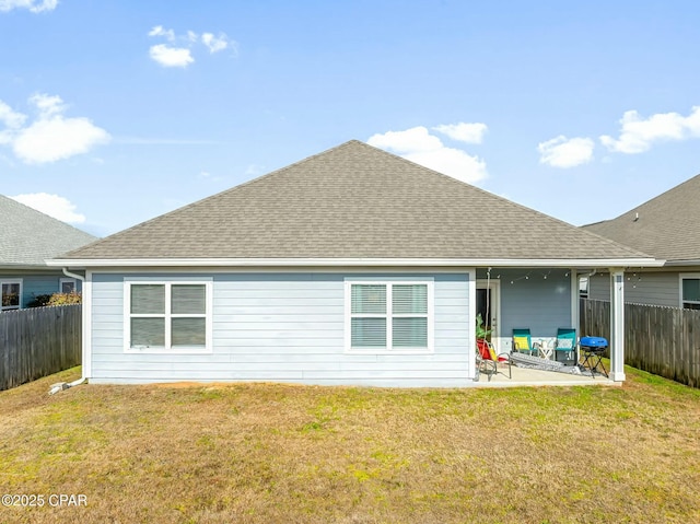rear view of house featuring a yard, a patio, a shingled roof, and fence
