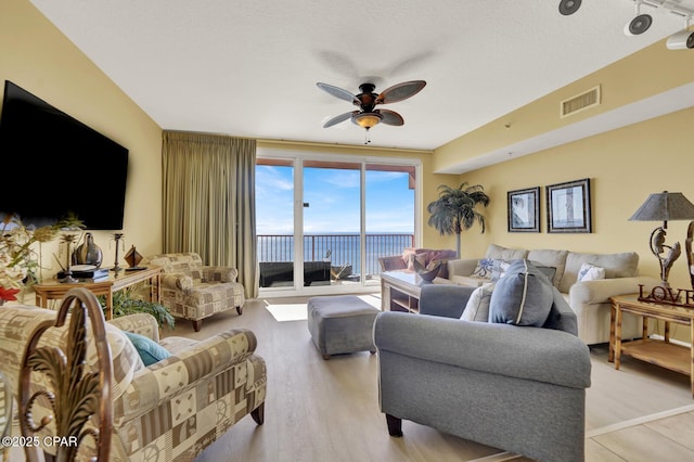 living room with a ceiling fan, a water view, light wood-style flooring, and visible vents