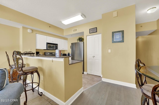 kitchen featuring a breakfast bar, visible vents, white cabinets, a peninsula, and appliances with stainless steel finishes