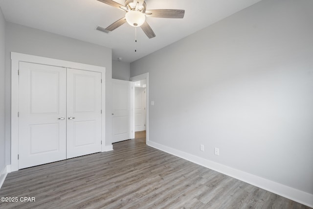 unfurnished bedroom with a closet, visible vents, baseboards, and wood finished floors