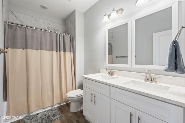 bathroom featuring double vanity, wood finished floors, toilet, and a sink