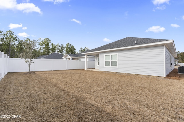 rear view of house featuring central air condition unit, a fenced backyard, a lawn, and roof with shingles