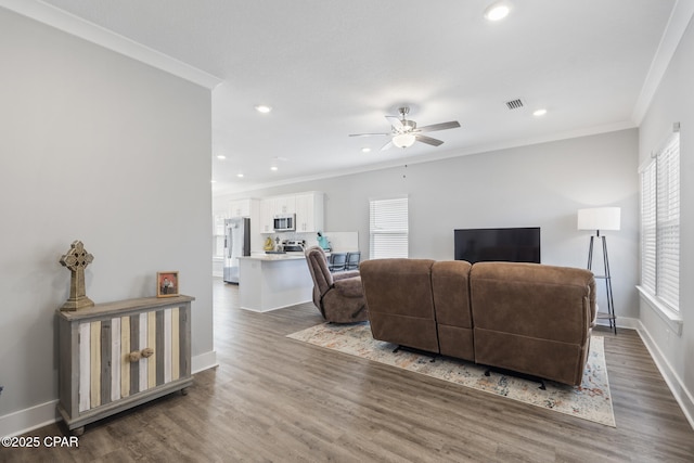 living area with crown molding, plenty of natural light, wood finished floors, and visible vents