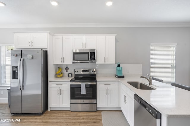 kitchen featuring backsplash, appliances with stainless steel finishes, a peninsula, light wood-style floors, and a sink