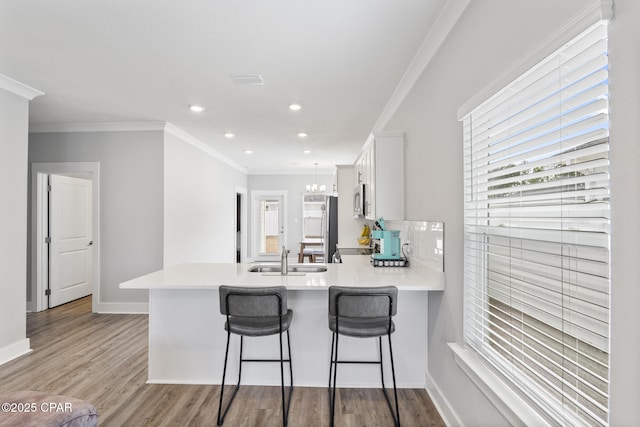 kitchen with a sink, stainless steel microwave, a peninsula, crown molding, and light countertops