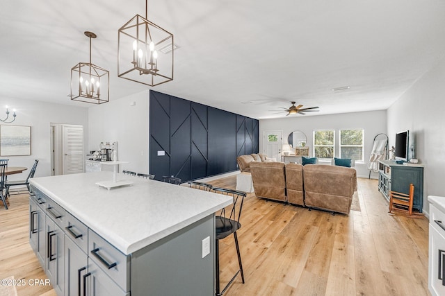 kitchen featuring a center island, hanging light fixtures, light wood-type flooring, gray cabinets, and ceiling fan with notable chandelier