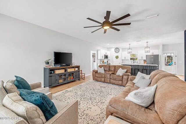 living room with ceiling fan, sink, and light wood-type flooring