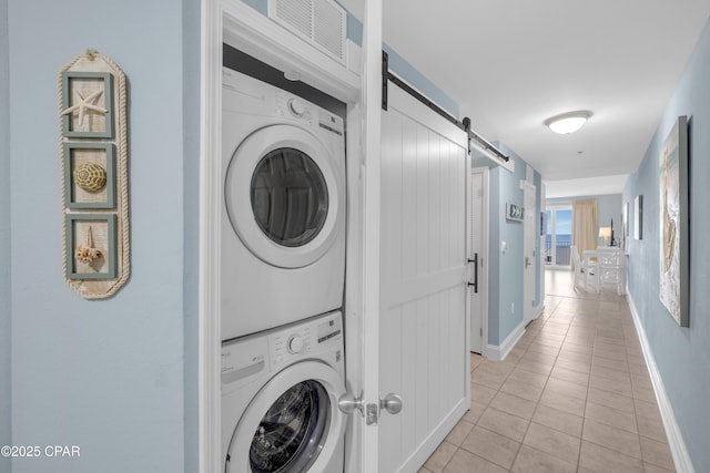 laundry area featuring light tile patterned floors, stacked washer and clothes dryer, and a barn door