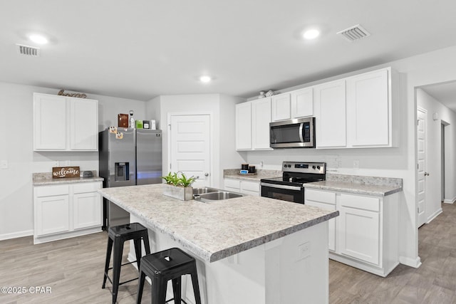 kitchen with stainless steel appliances, a kitchen island with sink, and white cabinets