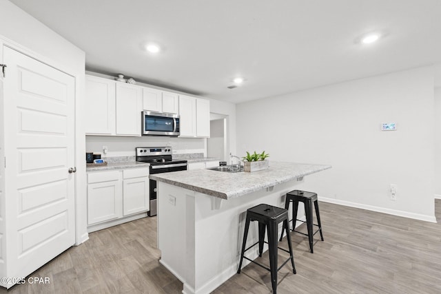 kitchen with a kitchen island with sink, white cabinetry, a breakfast bar area, and appliances with stainless steel finishes