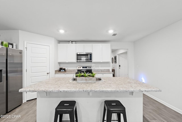 kitchen featuring a kitchen bar, an island with sink, white cabinets, and appliances with stainless steel finishes