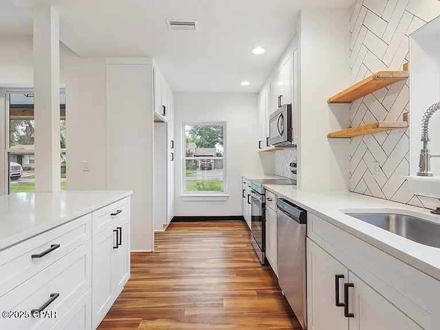 kitchen featuring sink, hardwood / wood-style flooring, appliances with stainless steel finishes, white cabinetry, and backsplash