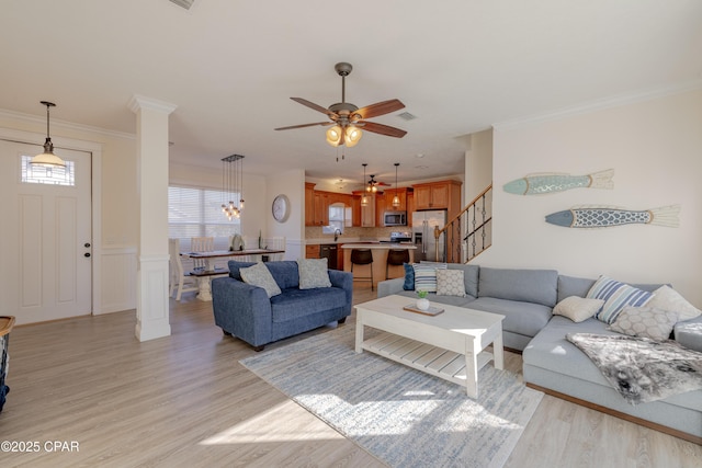 living room featuring ceiling fan, ornamental molding, decorative columns, and light wood-type flooring