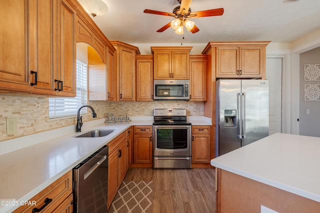 kitchen featuring appliances with stainless steel finishes, wood-type flooring, sink, backsplash, and ceiling fan