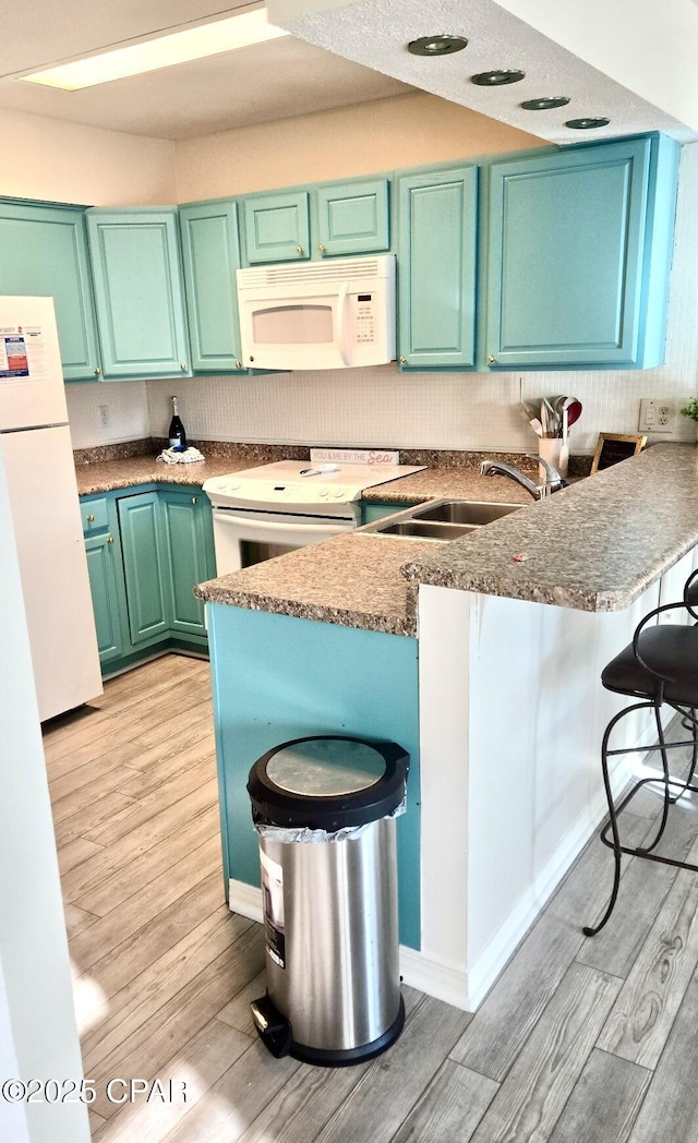 kitchen featuring a peninsula, white appliances, a kitchen bar, and a sink