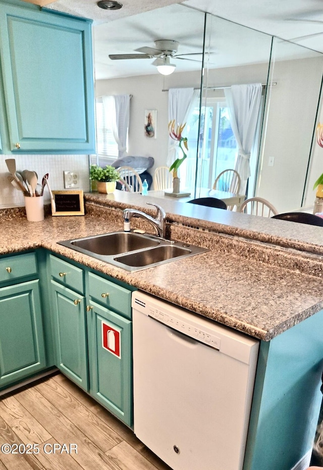 kitchen featuring a ceiling fan, a peninsula, white dishwasher, light wood-type flooring, and a sink