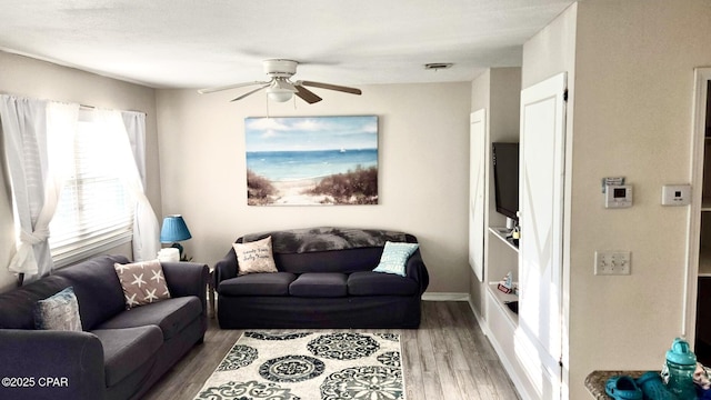 living area with baseboards, ceiling fan, visible vents, and wood finished floors