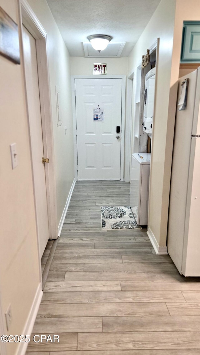 corridor with stacked washer / dryer, light wood-type flooring, and baseboards