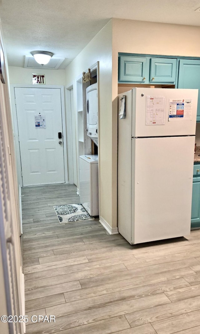 kitchen featuring light wood finished floors, stacked washer and clothes dryer, a textured ceiling, and freestanding refrigerator