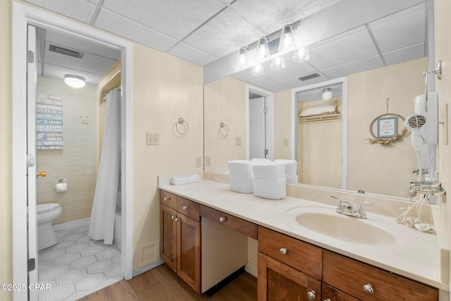 full bathroom featuring hardwood / wood-style floors, vanity, toilet, shower / bath combo, and a drop ceiling