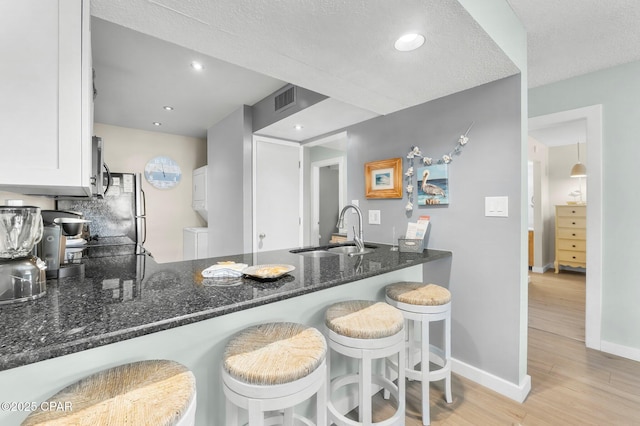 kitchen featuring sink, white cabinets, a kitchen breakfast bar, dark stone counters, and light hardwood / wood-style floors