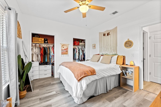 bedroom featuring two closets, light hardwood / wood-style floors, and ceiling fan