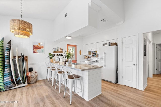 kitchen with a breakfast bar, hanging light fixtures, kitchen peninsula, white appliances, and white cabinets