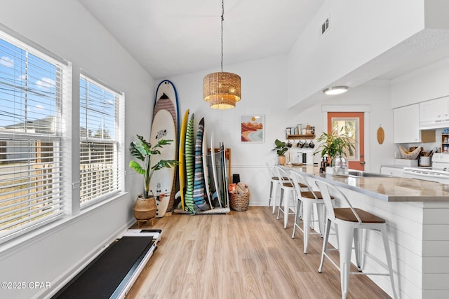 kitchen featuring pendant lighting, white cabinetry, a kitchen bar, white electric stove, and light wood-type flooring