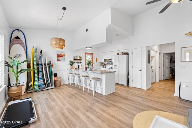 kitchen featuring white cabinetry, a kitchen breakfast bar, hanging light fixtures, white refrigerator with ice dispenser, and kitchen peninsula