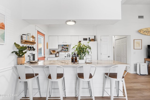 kitchen with a breakfast bar, white appliances, light stone countertops, light hardwood / wood-style floors, and white cabinets