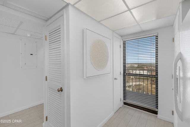 doorway featuring electric panel, a paneled ceiling, baseboards, and light wood finished floors