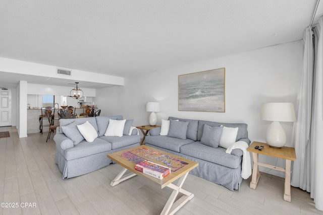 living room with an inviting chandelier, visible vents, and light wood finished floors