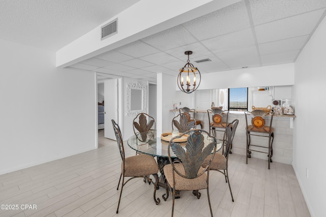 dining room featuring light wood finished floors, visible vents, a paneled ceiling, and an inviting chandelier