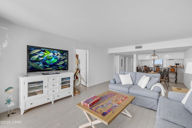 living area featuring a textured ceiling, light wood-style floors, visible vents, and a chandelier