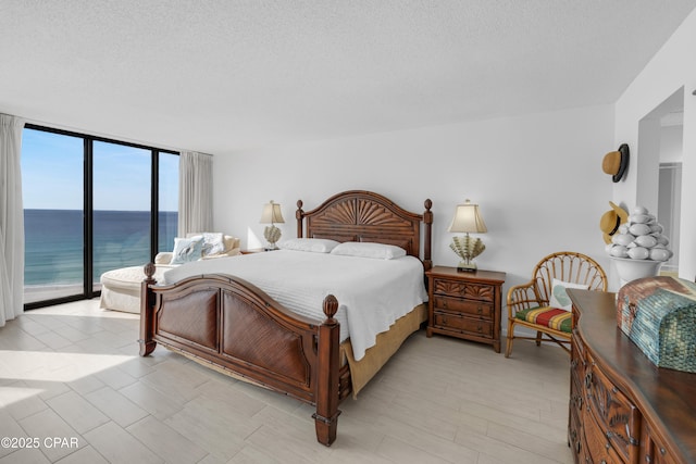 bedroom with a water view, expansive windows, access to exterior, and a textured ceiling